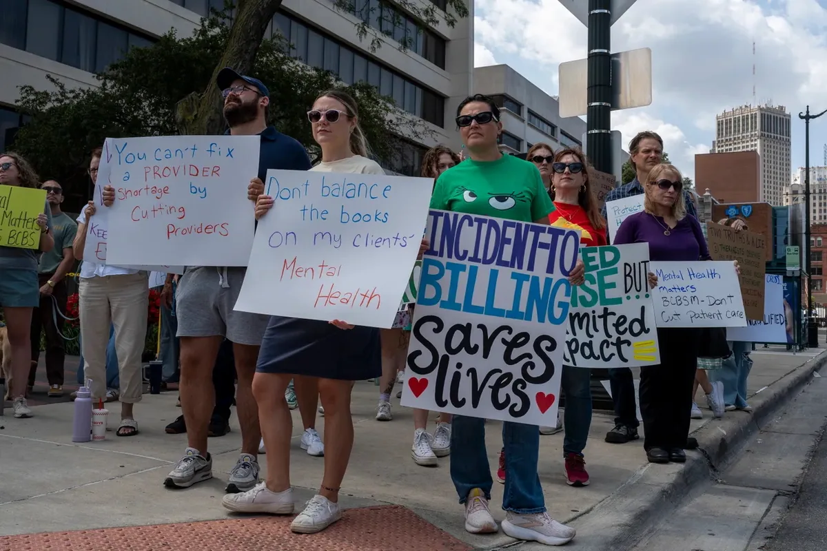 Demonstrators stand along a sidewalk holding hand-lettered signs reading "You can't fix a provider shortage by cutting providers" and "Incident-to billing saves lives."