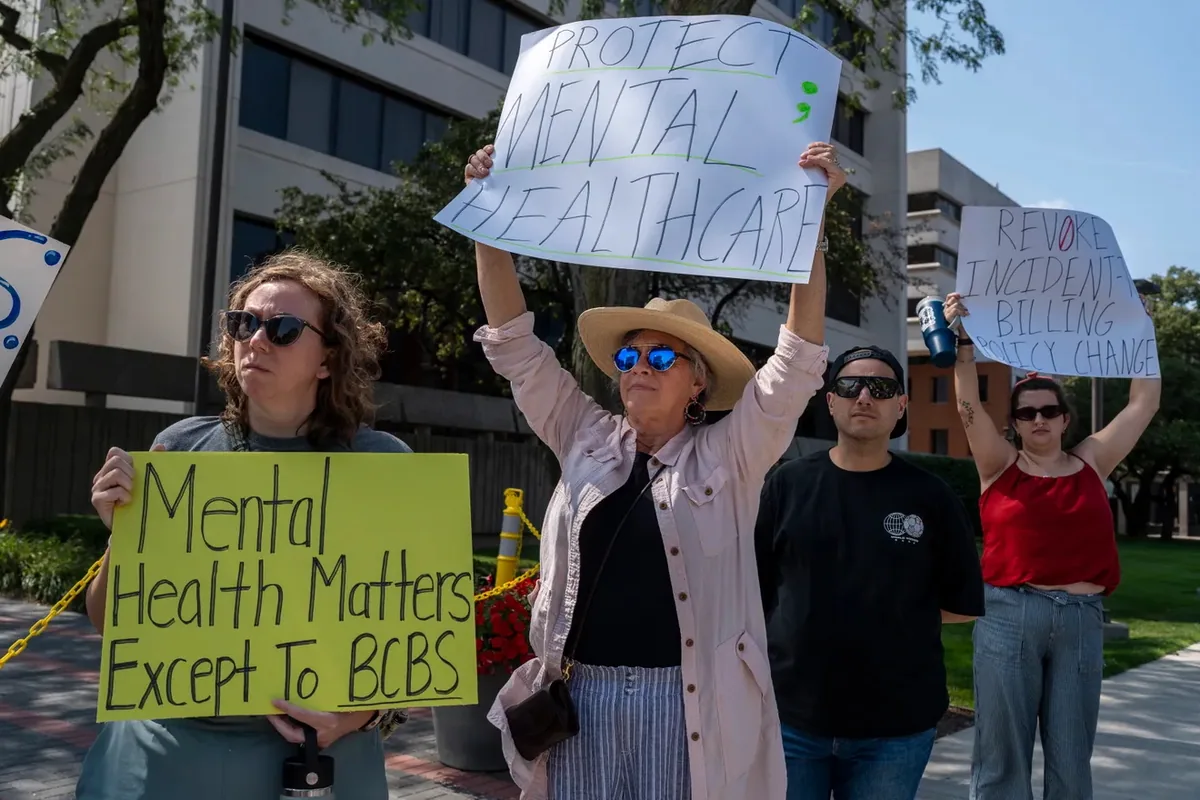 Four demonstrators hold signs including one reading "Mental Health Matters Except To BCBS" and one held overhead reading "PROTECT MENTAL HEALTHCARE."